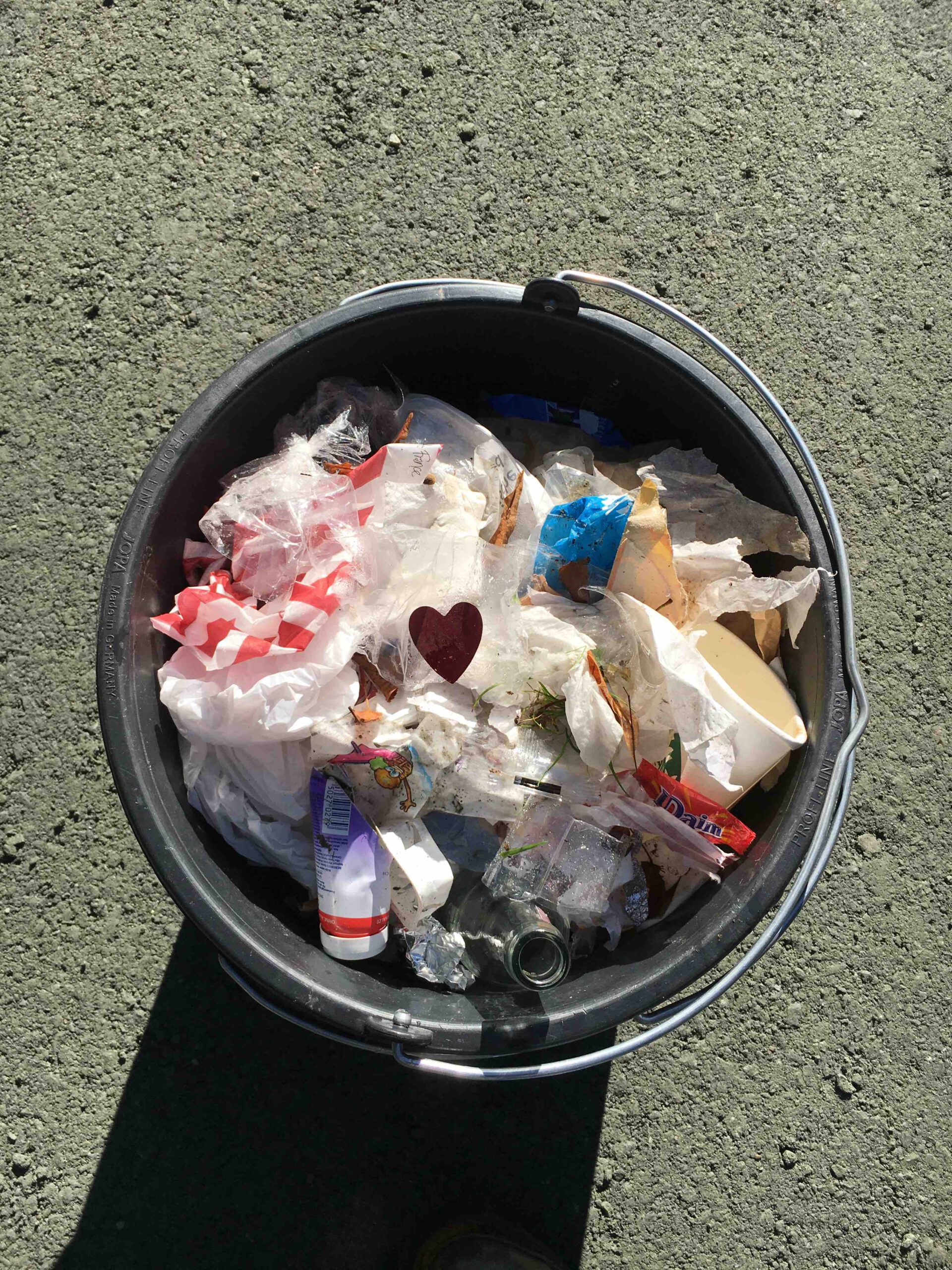 Ein voller Mülleimer mit einem roten Konfetti-Herz auf der Mitte des Mülls.