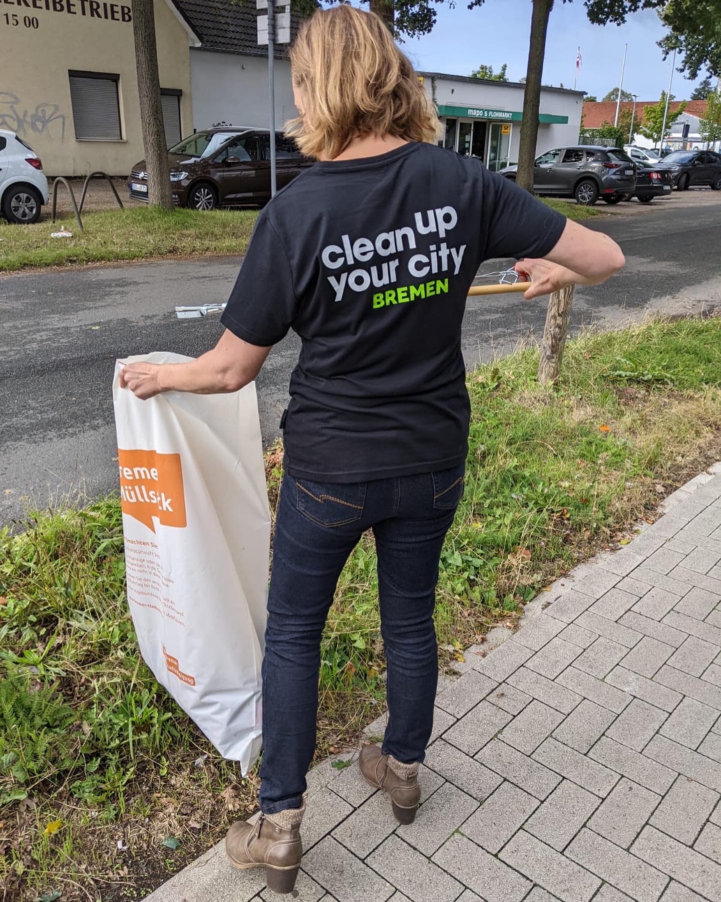 Eine Frau mit einem Vereins-Shirt sammelt Müll in einen Bremer Müllsack